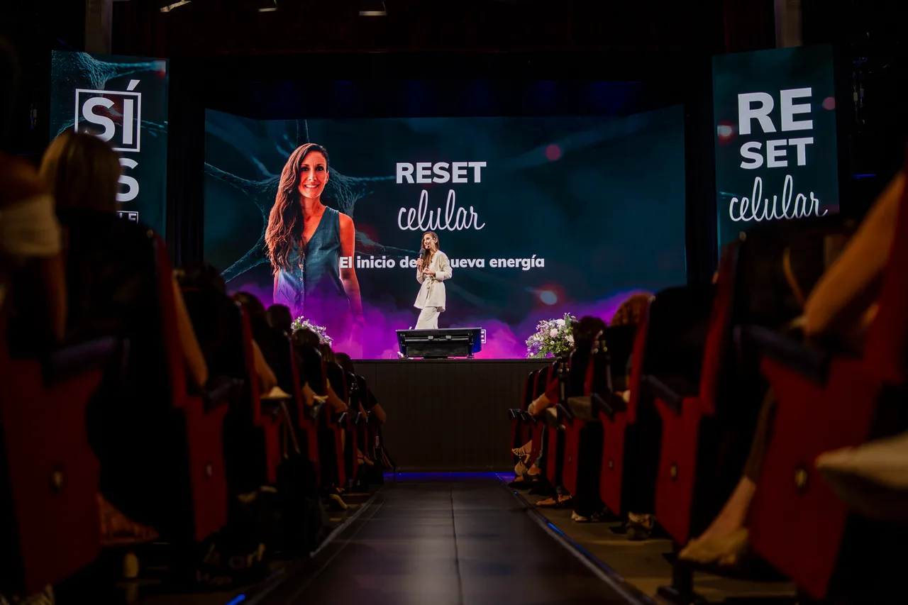 Ana Pedroche dando una conferencia en un teatro lleno, con la pantalla del escenario mostrando «Reset Celular»